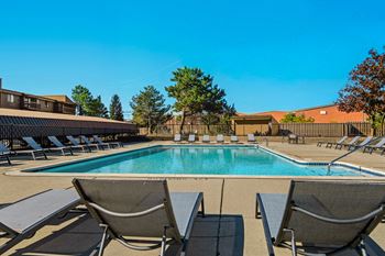 A pool surrounded by lounge chairs and trees.